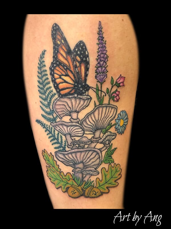 A colored tattoo of a butterfly surrounded by mushrooms and flowers