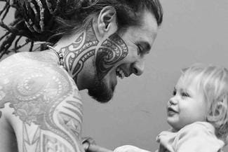 A picture of a man with tattoos posing with a toddler