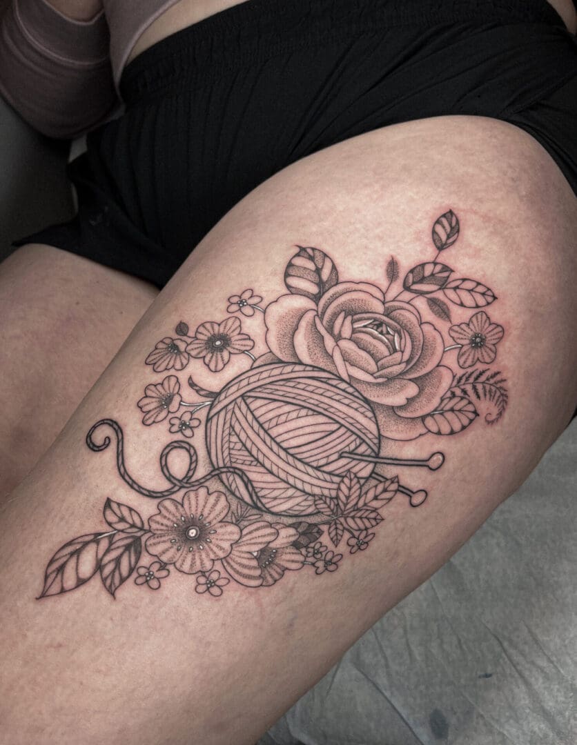 A woman 's leg with a tattoo of yarn and flowers.